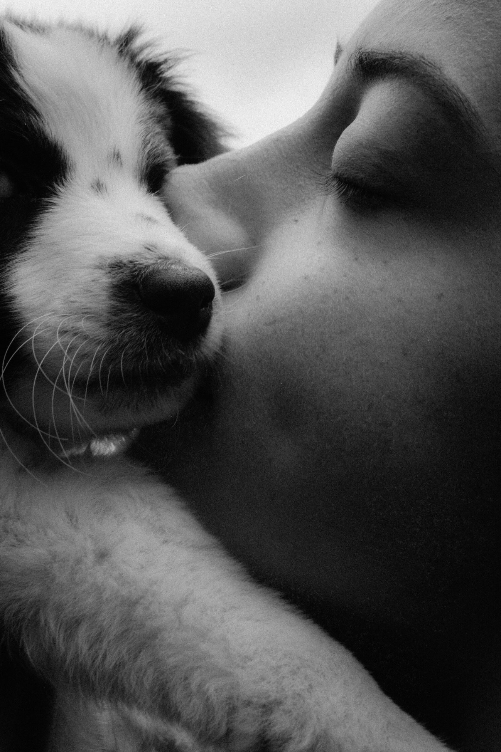 Close-up black and white photo of a woman affectionately kissing a puppy.