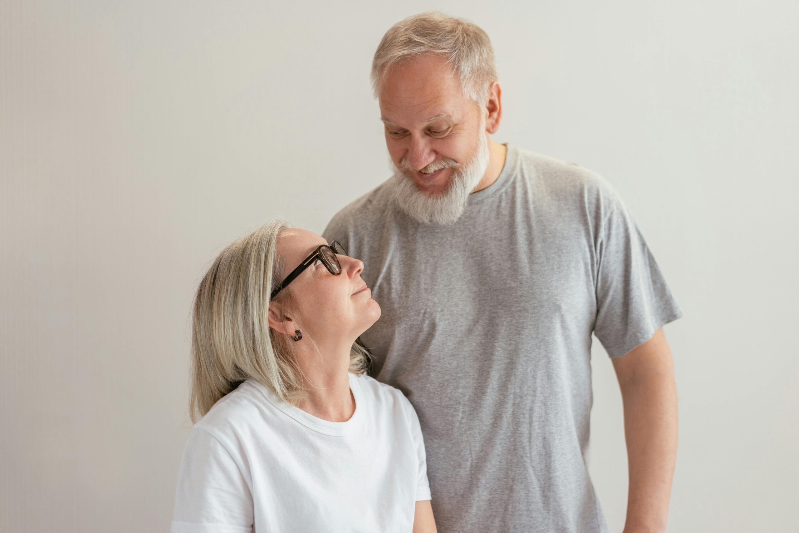 Elderly couple with eyeglasses and beards sharing a joyful moment indoors.